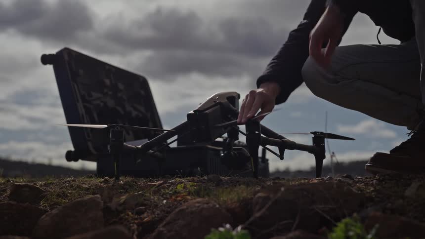 A man stands on a cliff assembling a drone