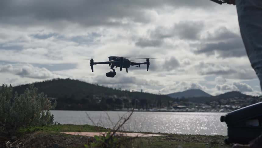 A drone lands on the sidewalk near the sea