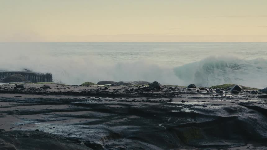 A view of ocean waves crashing against black rocks