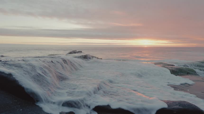 A small wave that follows a rock in a place with an ocean on the horizon one morning