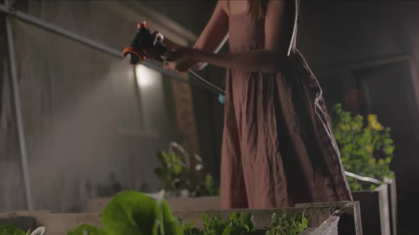 Woman waters raised garden beds placed near house at night