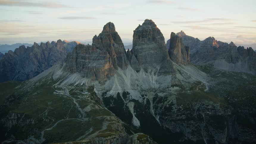 Paths wind over slopes of jagged mountain in rugged terrain at sunrise