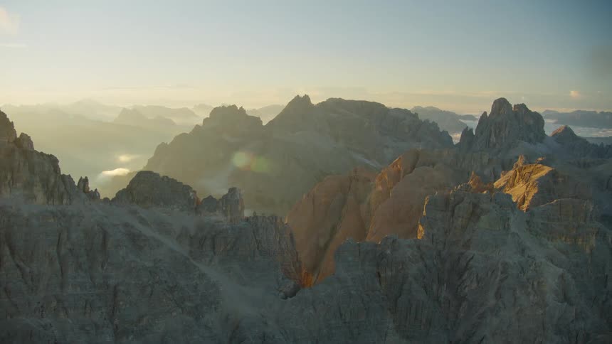 A view of a mountain range with peak formations and cliffs during a sunrise