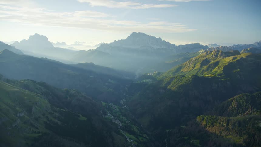 An aerial view of a landscape with mountains and hills covered in forests and green grass