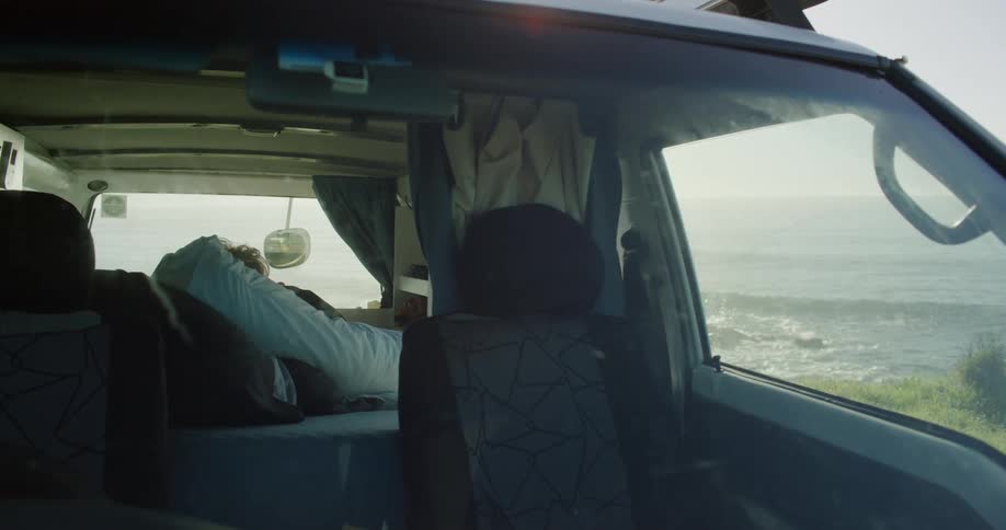 Someone sleeps in a car parked in front of the sea at midday