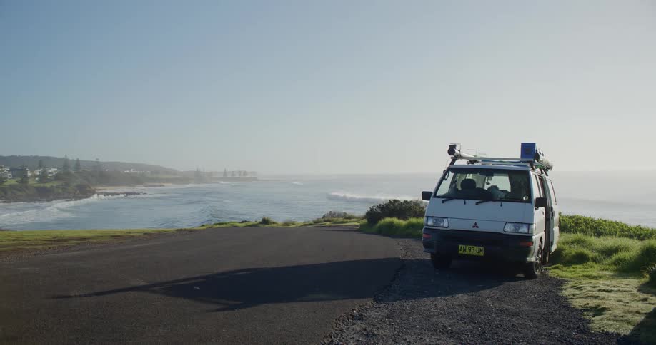 A small van parked near the sea shore where the waves are breaking