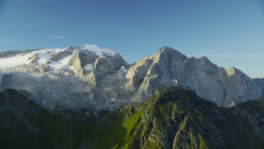 A mountain peak with snow and another mountain covered with grass
