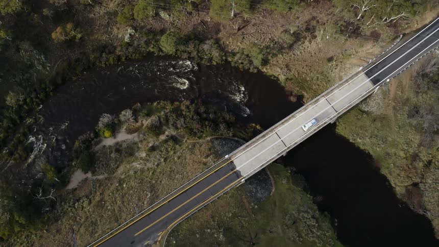 Vehicle drives under power lines and across bridge over river in countryside
