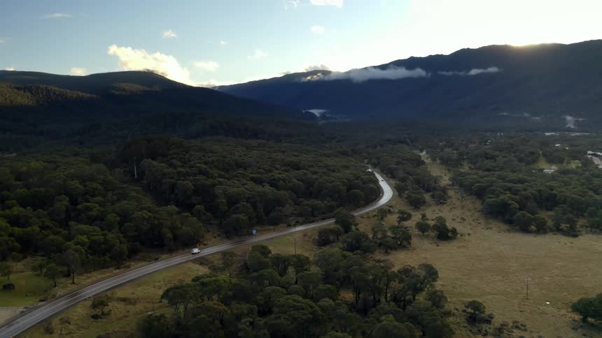 An aerial view of a road through a natural environment with mountains and trees