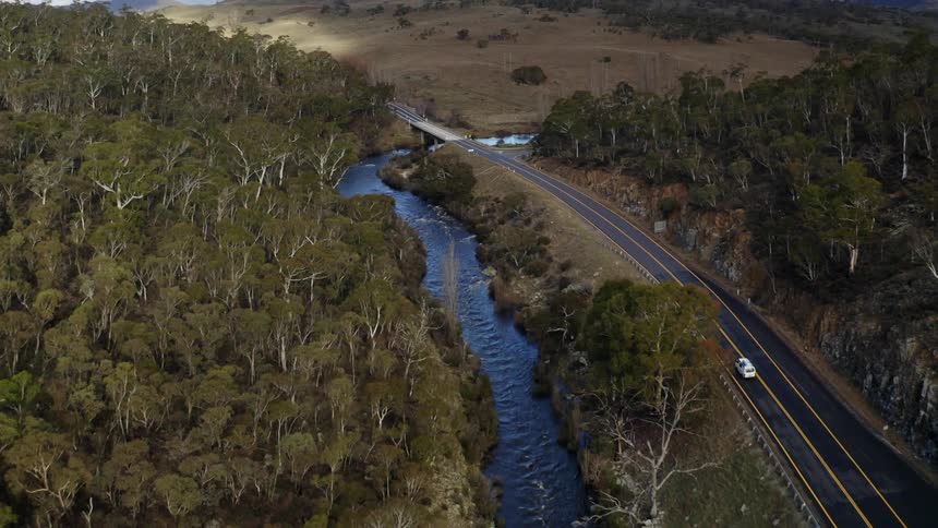 Van drives along highway partially paralleling river through forest