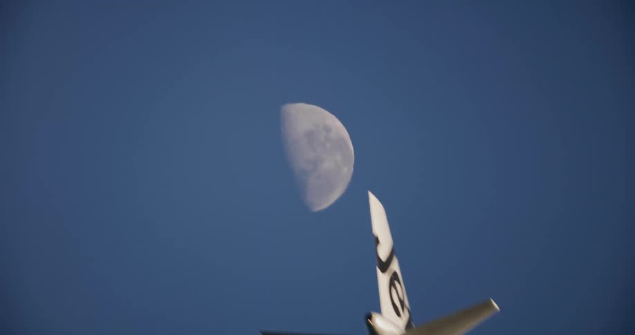 An airplain flying close to the ground during dawn with the moon still visible and the sun shining