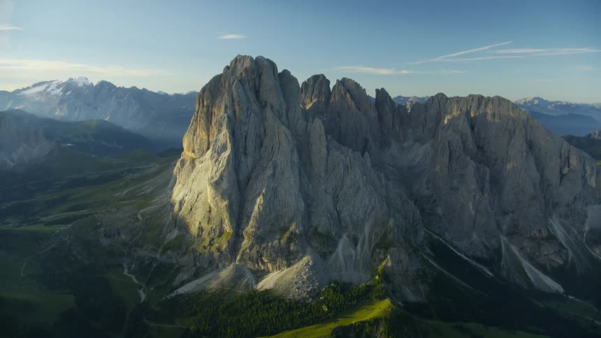 An aerial view of a mountain range valley and cliffs with lush vegetation at the base and rocky peaks