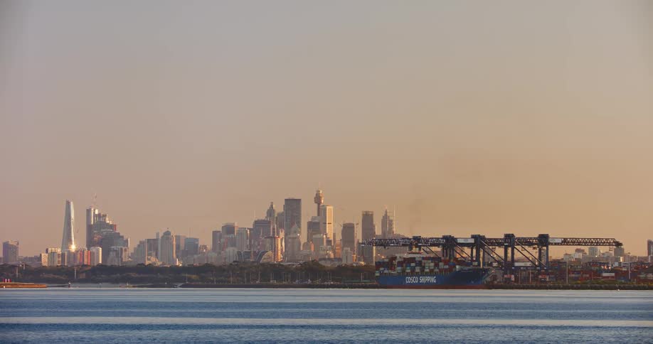 A distant view of a metropolis by the sea with a cargo ship and an orange sky