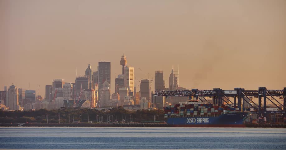 A boat is at the shipping dock along the coast with tall downtown buildings on the city skyline