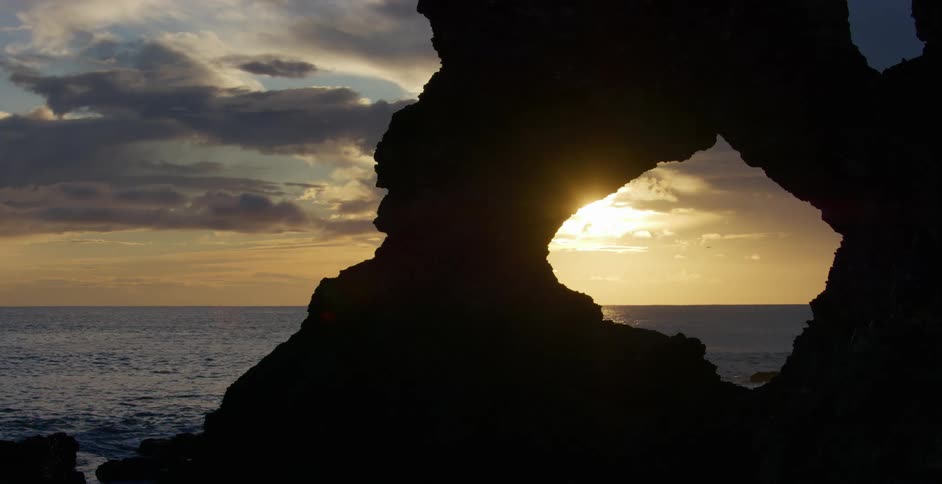 Sunset sun shines through a rock arch next to the ocean