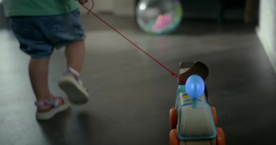 A toddler walking and playing with a toy car