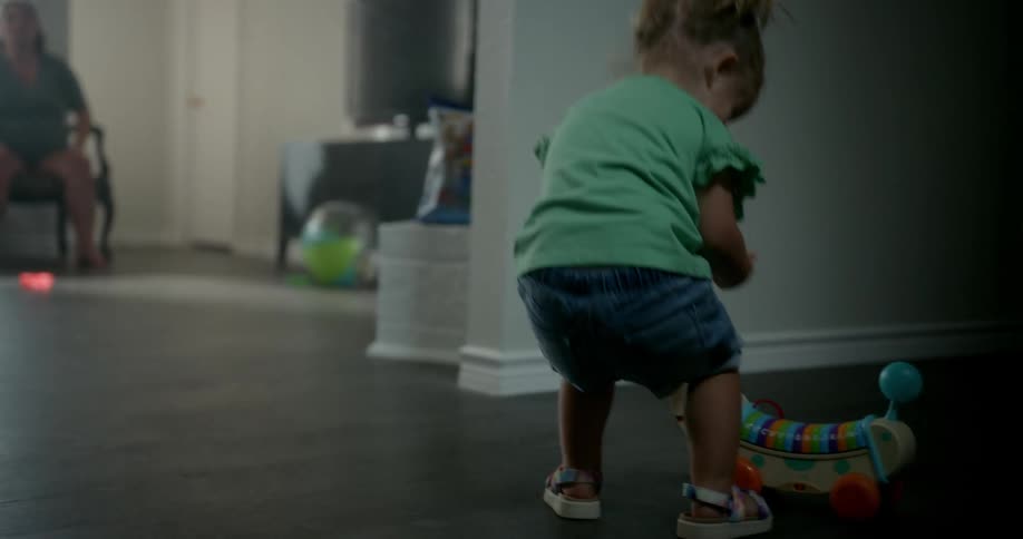 A girl stumbling and getting up heading towards her grandmother and picking up her toy