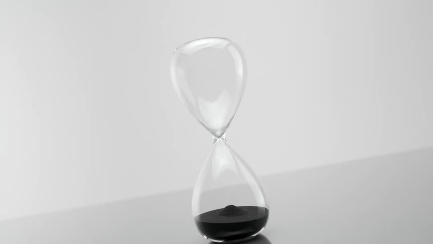 Black sand pours down inside a glass hourglass