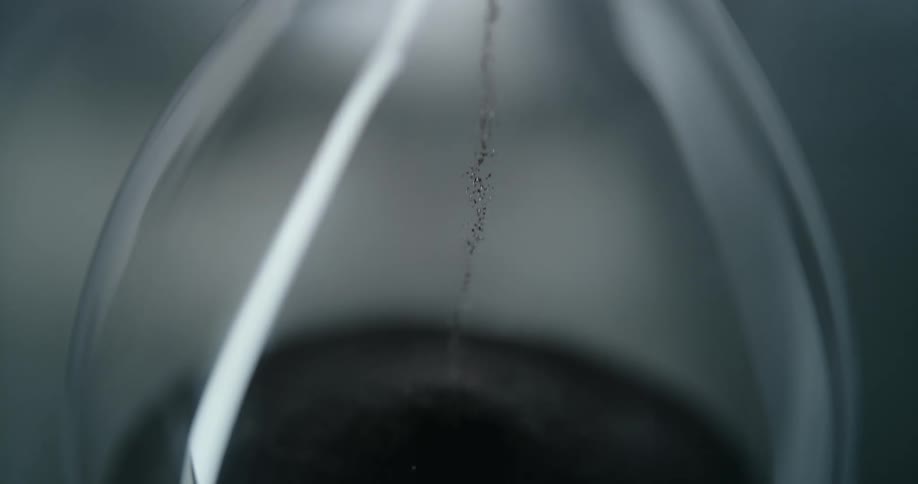Black sand falling from the glass hourglass
