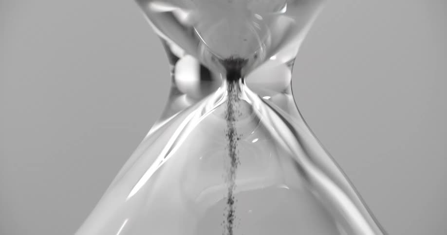 Small grains of sand falling in a pile inside a glass hourglass