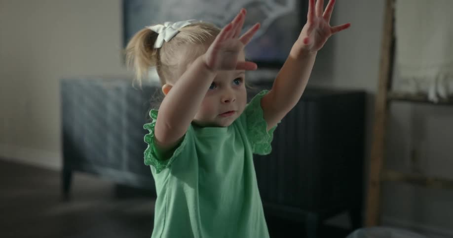 Girl child raised both hands up while standing indoor at midday
