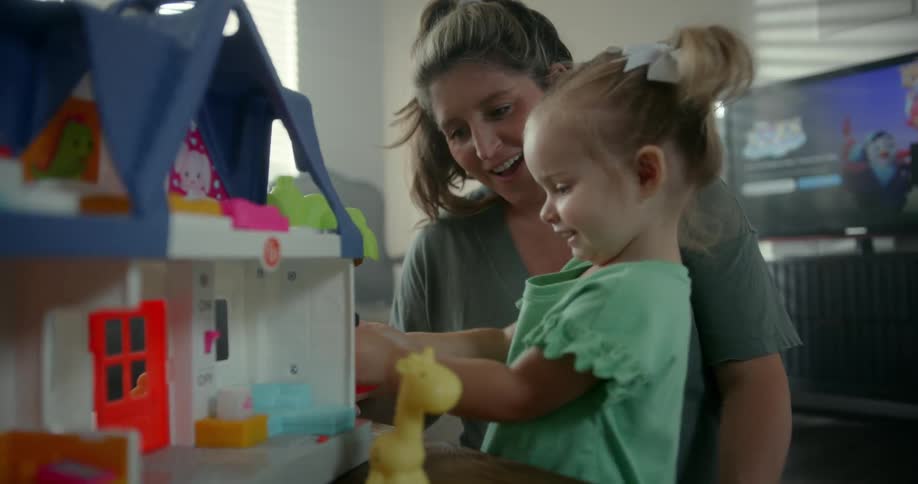 Mother playing with her daughter with a toy dollhouse