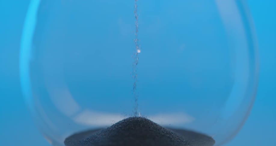 Sand flows through the center of an hourglass and falls into the pile at the bottom