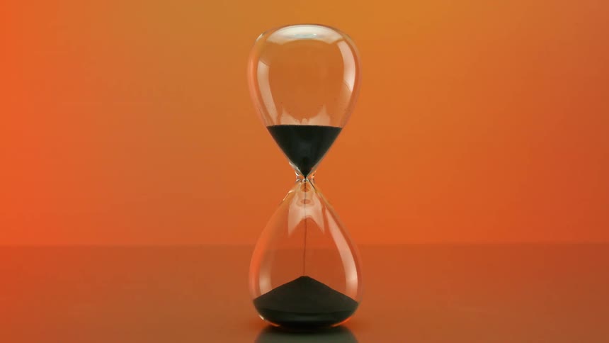 A glass hourglass with black sand falling down