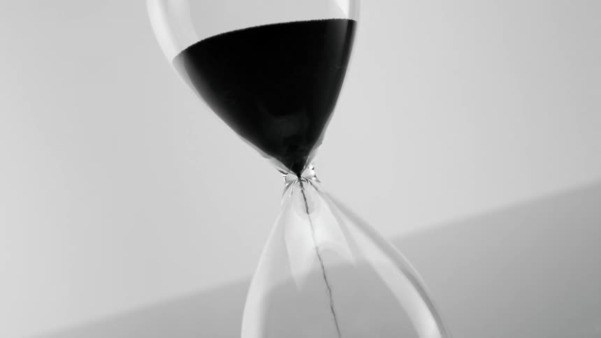 Hour glass with sand dripping placed on the ground