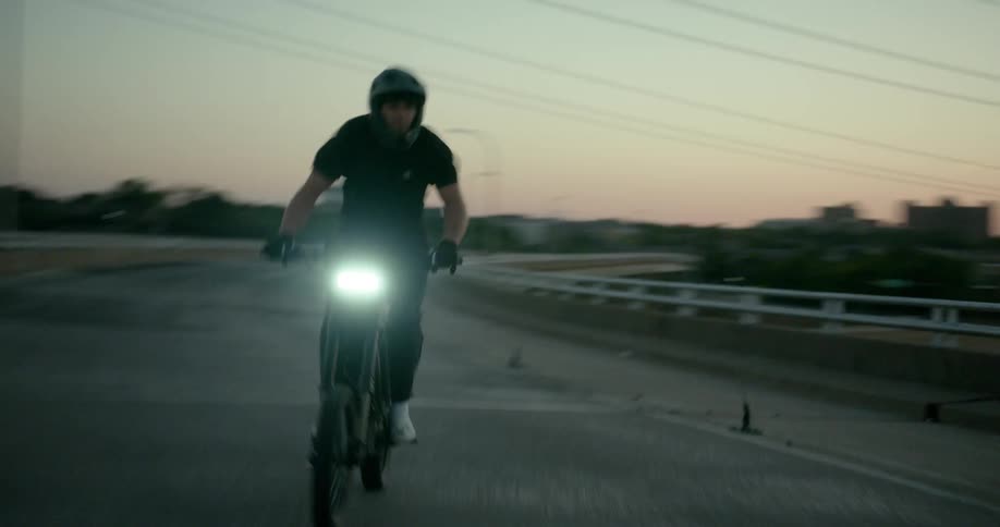 A man riding a motorcycle at high speed on a road in the late afternoon