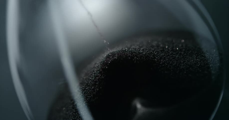 Some grains of sand falling in a pile inside a glass hourglass