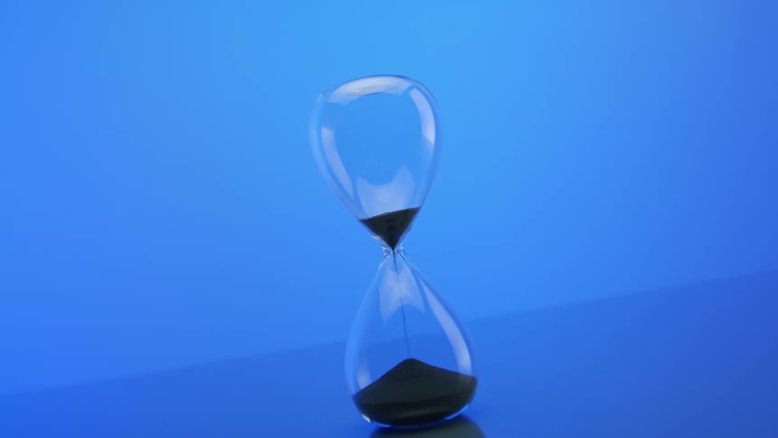 An hourglass with black sand being poured against a blue background