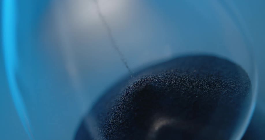 Small grains of sand falling in a pile inside a glass hourglass