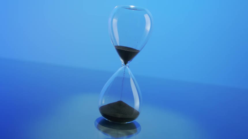 An hourglass where grains of sand are falling downwards in a blue background
