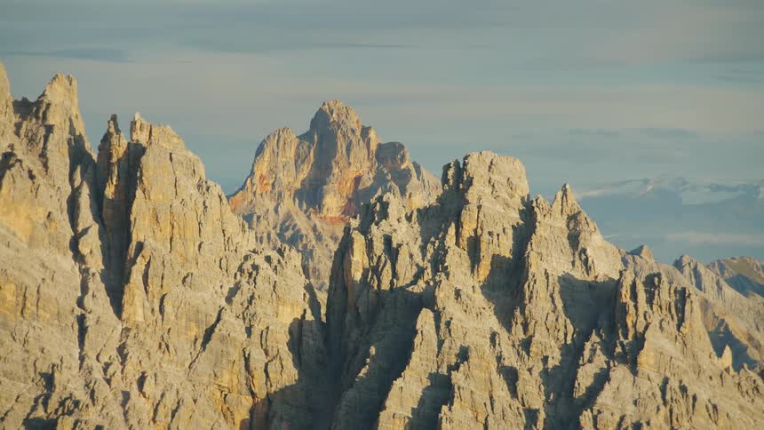 The sun shines upon rough jagged dolomite mountains under a cloudy sky