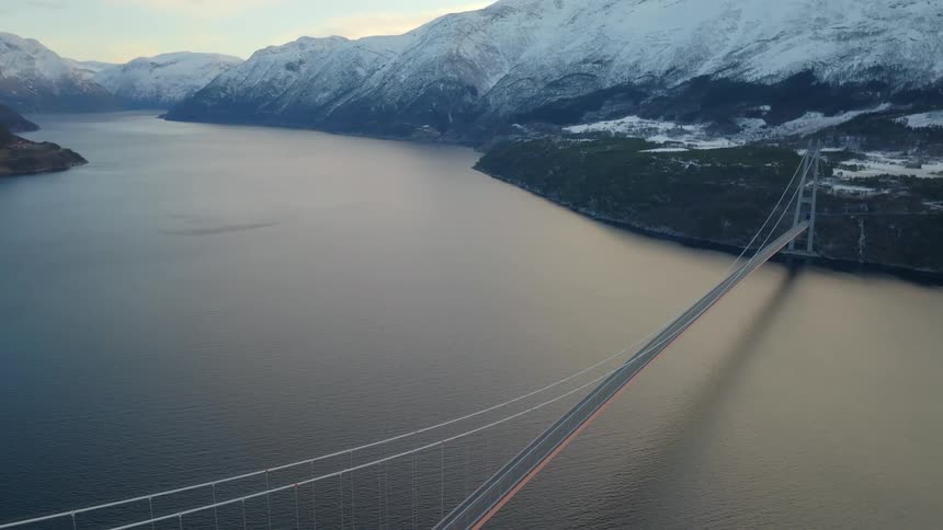 A view of a massive bridge spanning a vast lake and connecting between snowcovered mountains