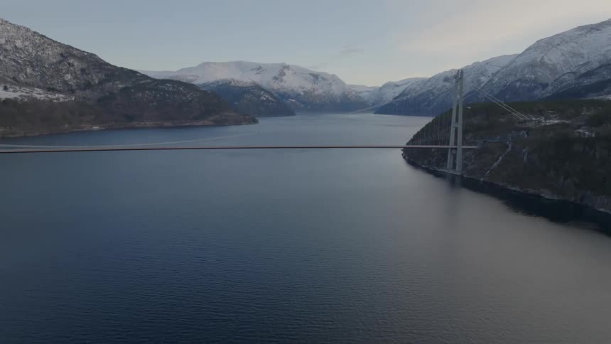 Aerial view of a massive bridge over a lake and snowcovered mountains