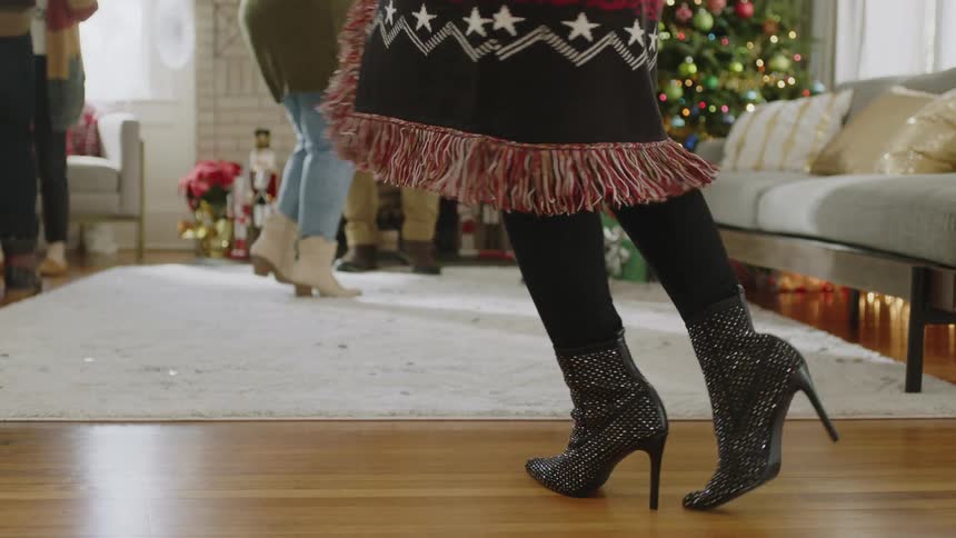 A woman shown from the waist down models sparkly shoes at a family holiday gathering