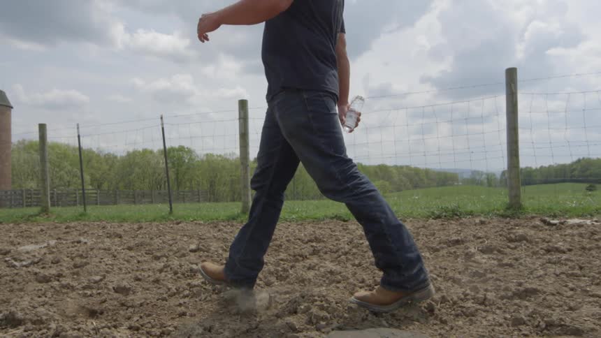 A man is walking in the dirt by a fence