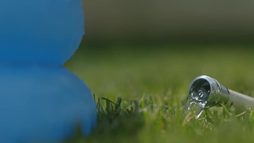 A stream of clear water is flowing from the silver nozzle of a white hose lying in some green grass next to a blue plastic inflatable