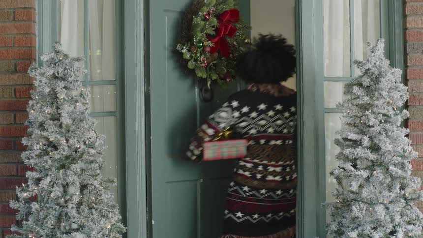 A woman with a gift in her hand knocks on the door then a boy appears and joyfully pulls her inside by the hand
