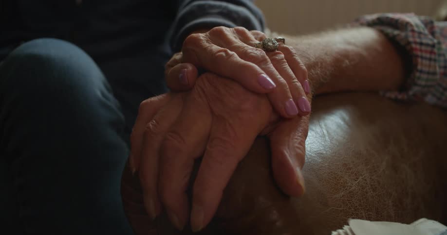A elderly woman puts her hand on an elderly man's arm