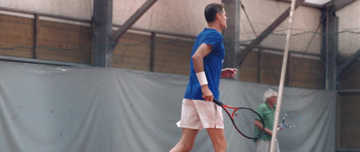 An adult man running with a tennis racket in his right hand