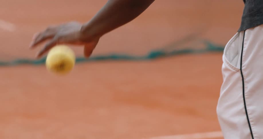 A closeup of a persons hands bouncing a tennis ball on the ground