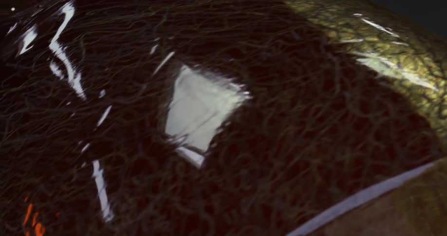 A shiny reflective glassy cylinder is rolling away from the camera bright squares windows and many intricate strands or fibersare reflected on its surface