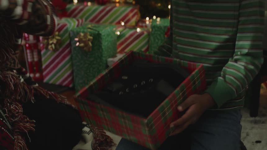 Mother hands the son a gift box containing shoe to open while the father watches