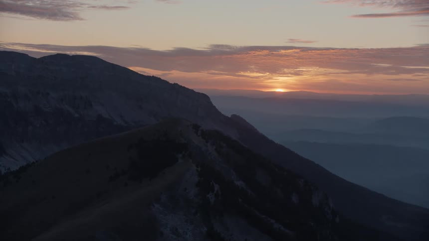 An aerial view of mountain peaks and the sunset shining in the sky