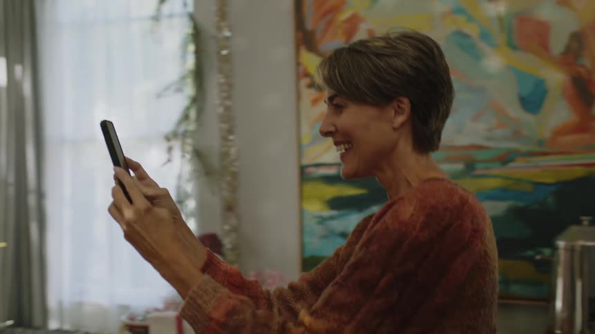 A young man and woman dance happily while a middleaged woman records them on a phone surrounded by christmas decorations