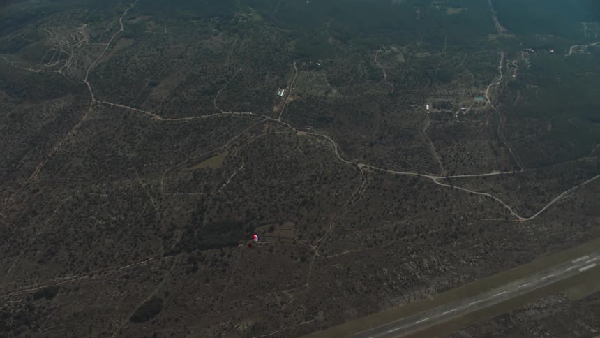 A person gliding with a red parachute on a terrain with several solar panels