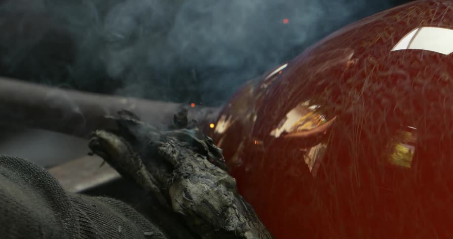 Closeup of a glass sphere undergoing the transition from its solid state to tempered glass with smoke emanating